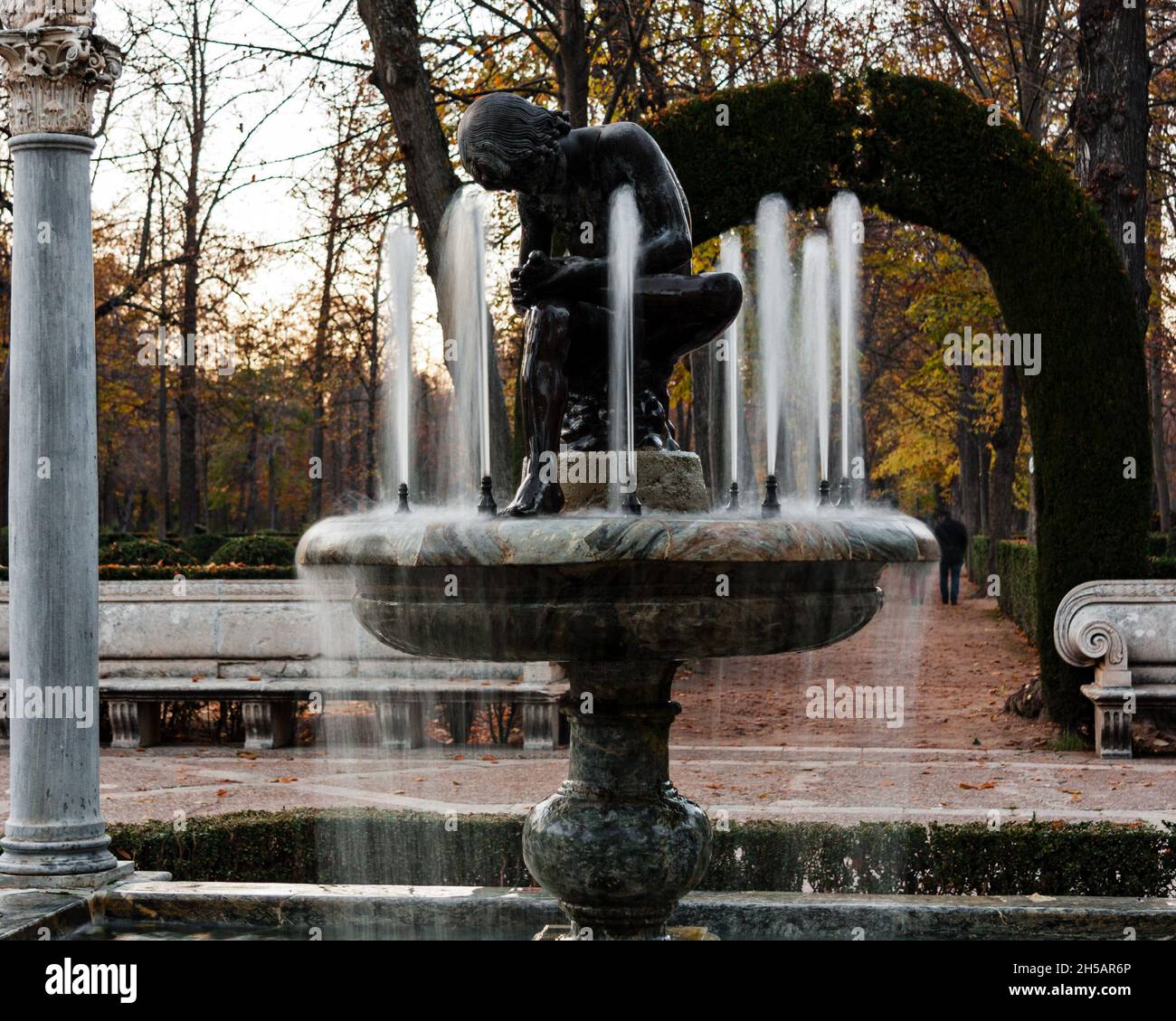 Fontaine avec sculpture d'un garçon touchant son pied située dans un jardin en automne.Format carré.Mise au point sélectionnée. Banque D'Images