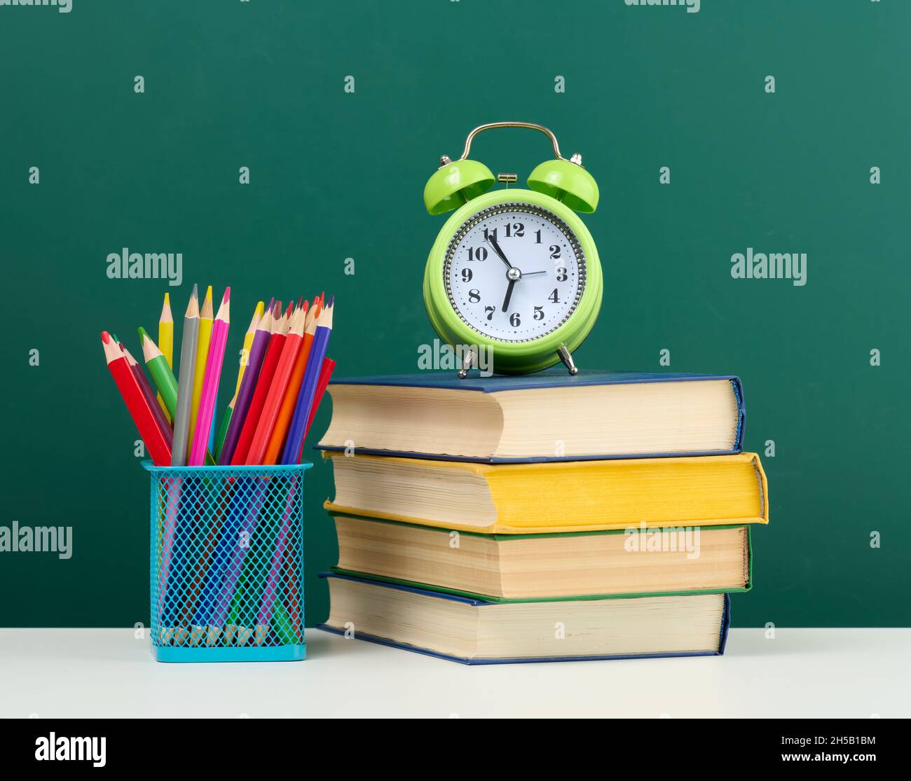 pile de livres, un réveil rond et des crayons multicolores sur le fond d'un tableau vert vide.Retour à l'école Banque D'Images