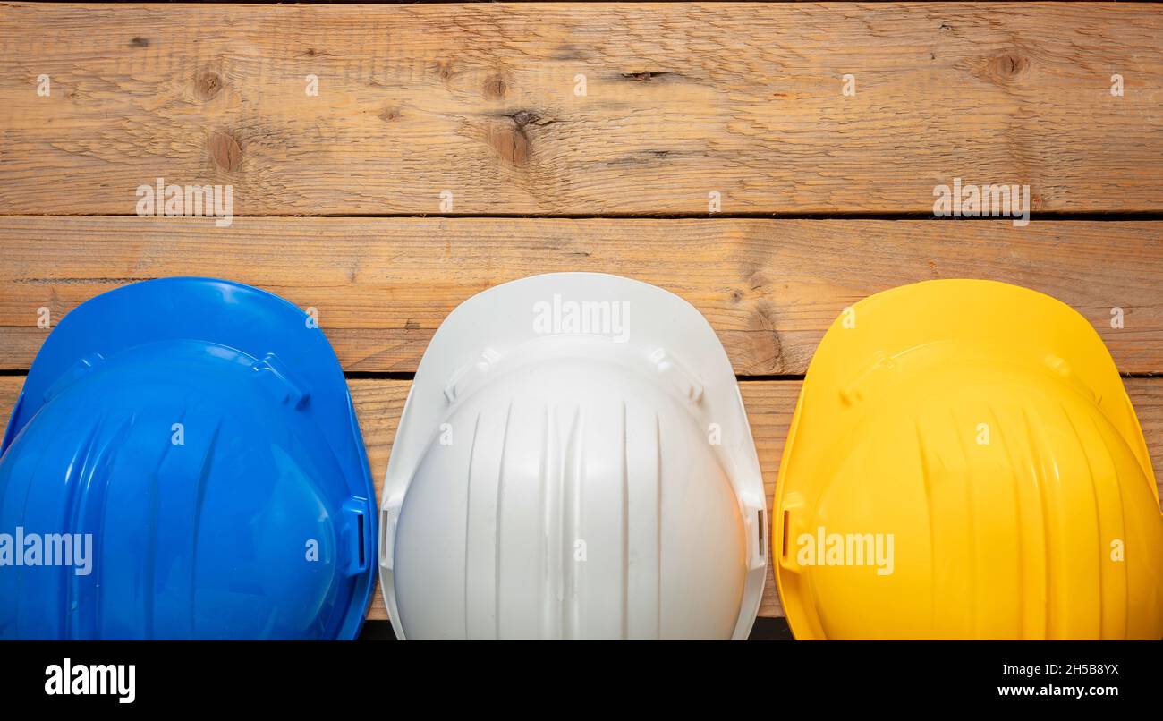Casques de sécurité, casques de sécurité blancs bleus et jaunes.Équipement de tête de protection individuelle pour chantier, fond en bois.Casques de sécurité pour les ingénieurs Banque D'Images