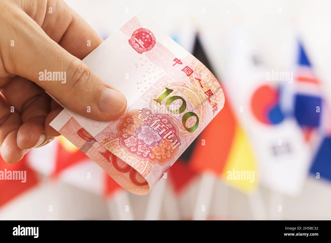 Cent yuan à la main sur fond de drapeaux de différents pays, gros plan Banque D'Images