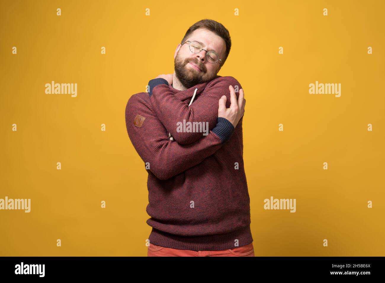 Charmant homme caucasien barbu dans des verres se bande tendly, fermant ses yeux de rêve.Arrière-plan jaune. Banque D'Images