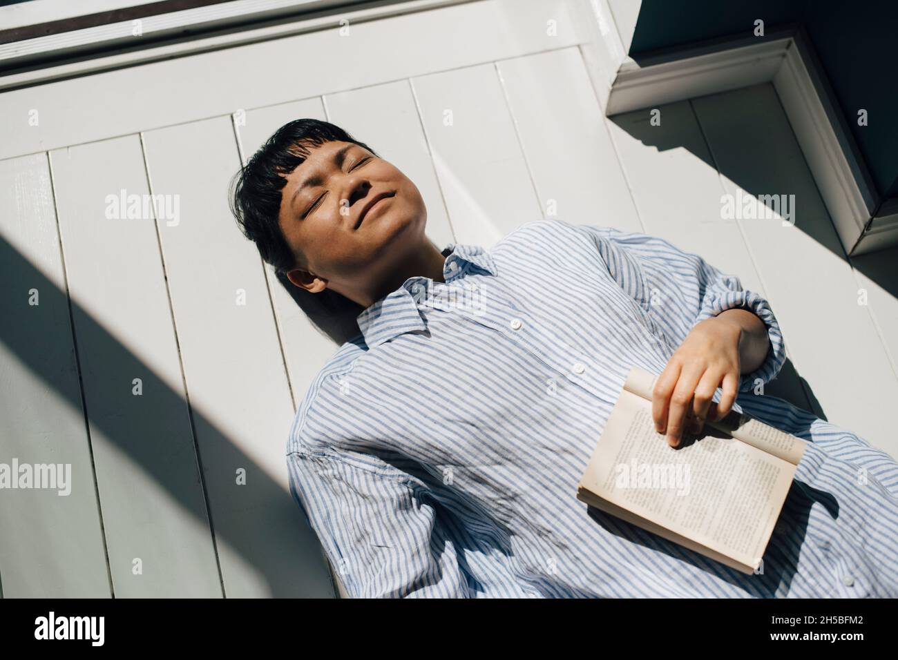 Jeune femme couché sur le sol avec livre à la lumière du soleil à la maison Banque D'Images