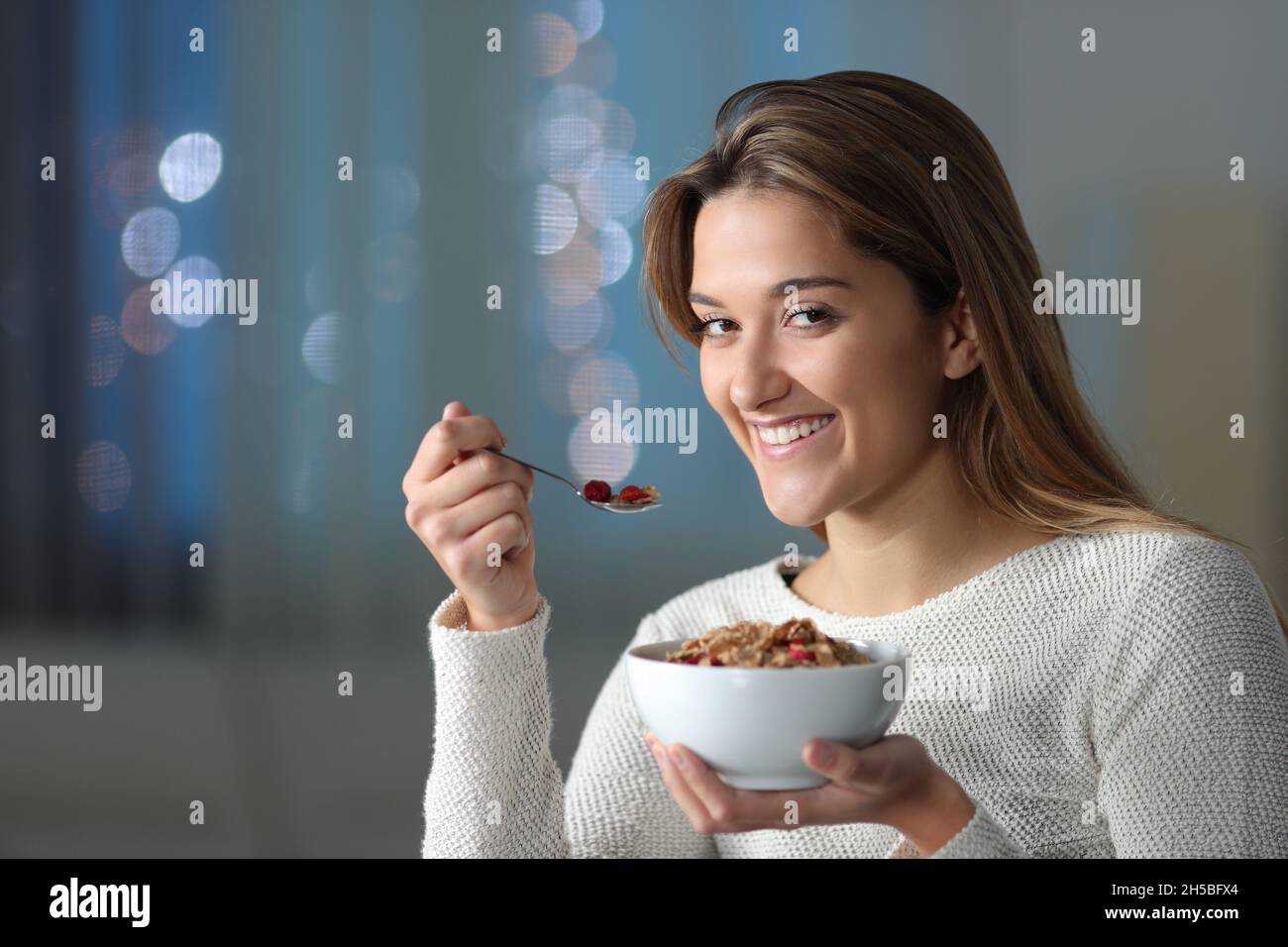 Bonne femme regardant l'appareil photo manger des céréales dans la nuit à la maison Banque D'Images