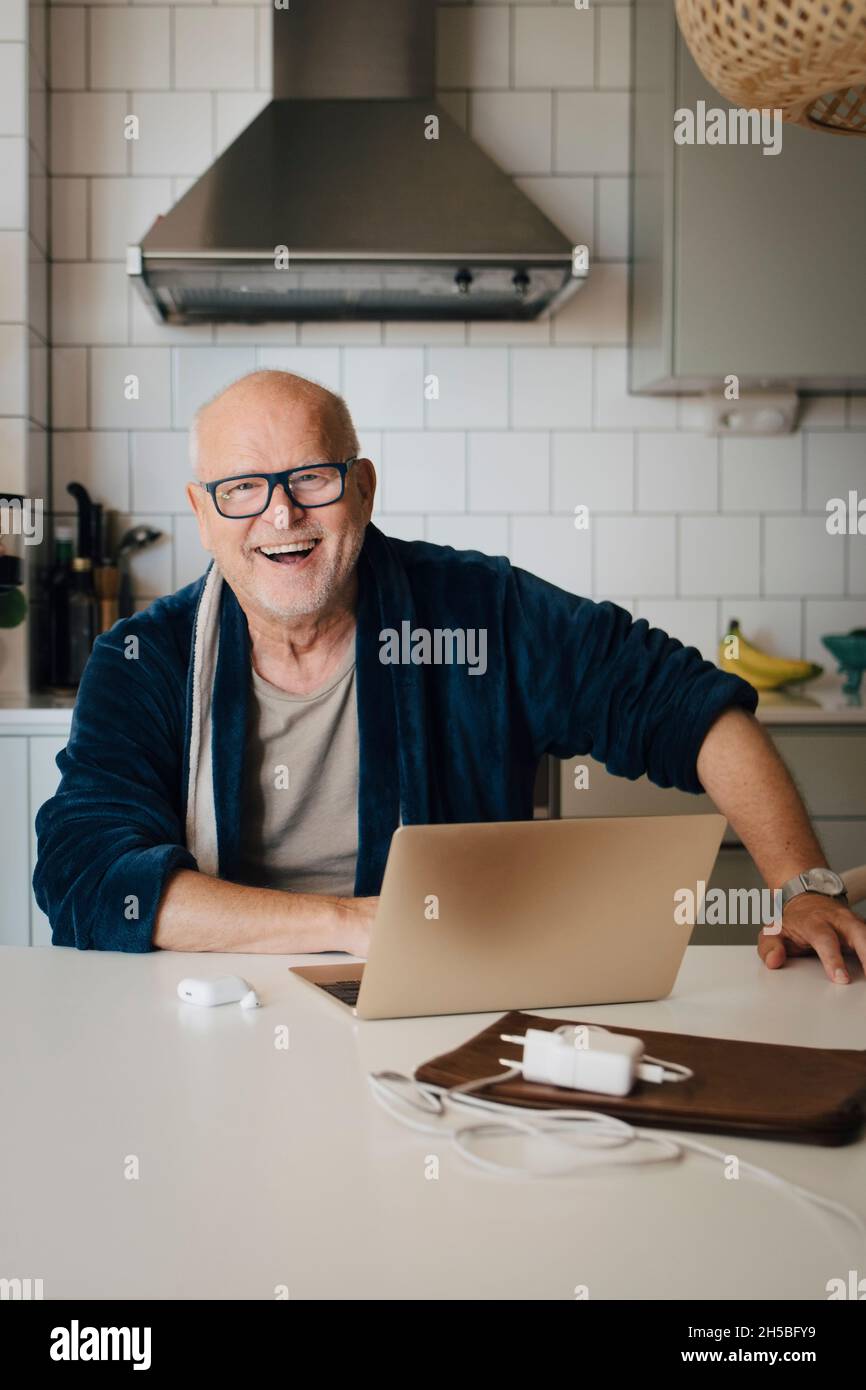 Portrait d'un homme âgé heureux avec ordinateur portable sur l'île de cuisine à la maison Banque D'Images