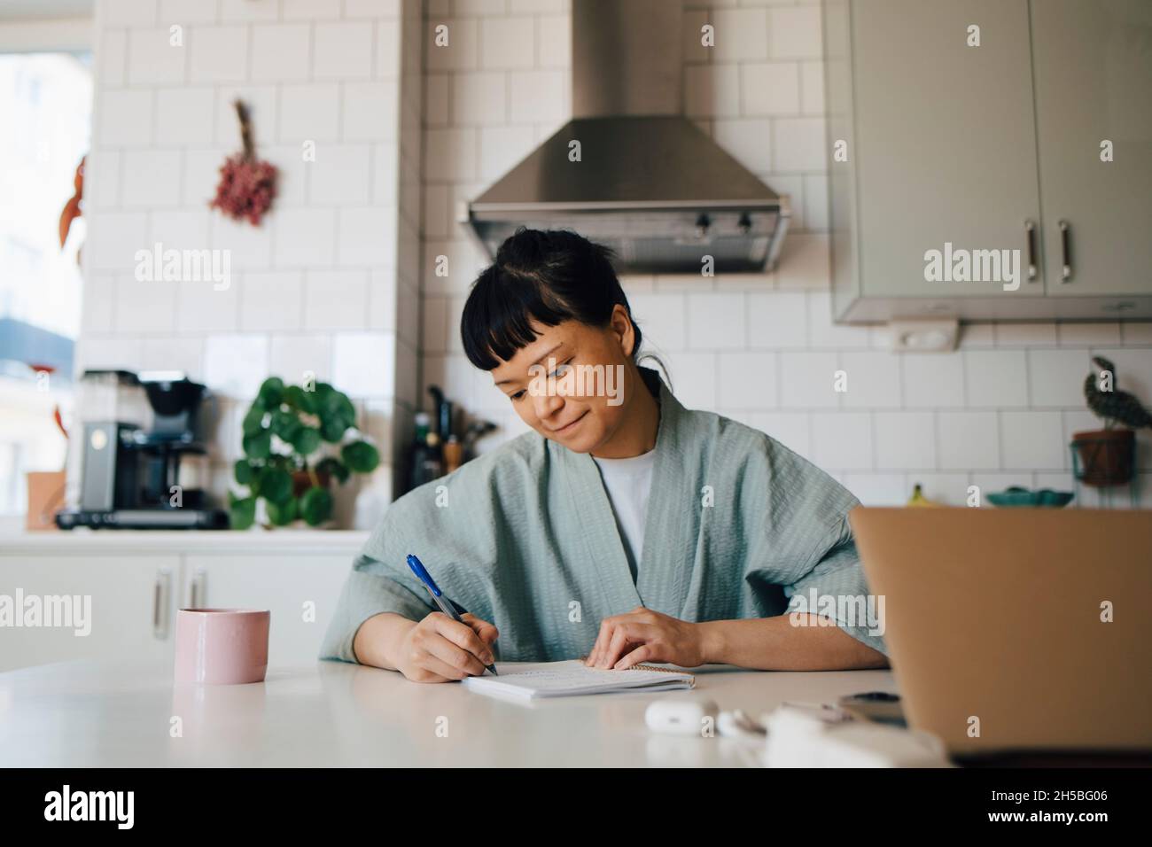 Jeune femme en peignoir écrivant dans le livre à la cuisine domestique Banque D'Images