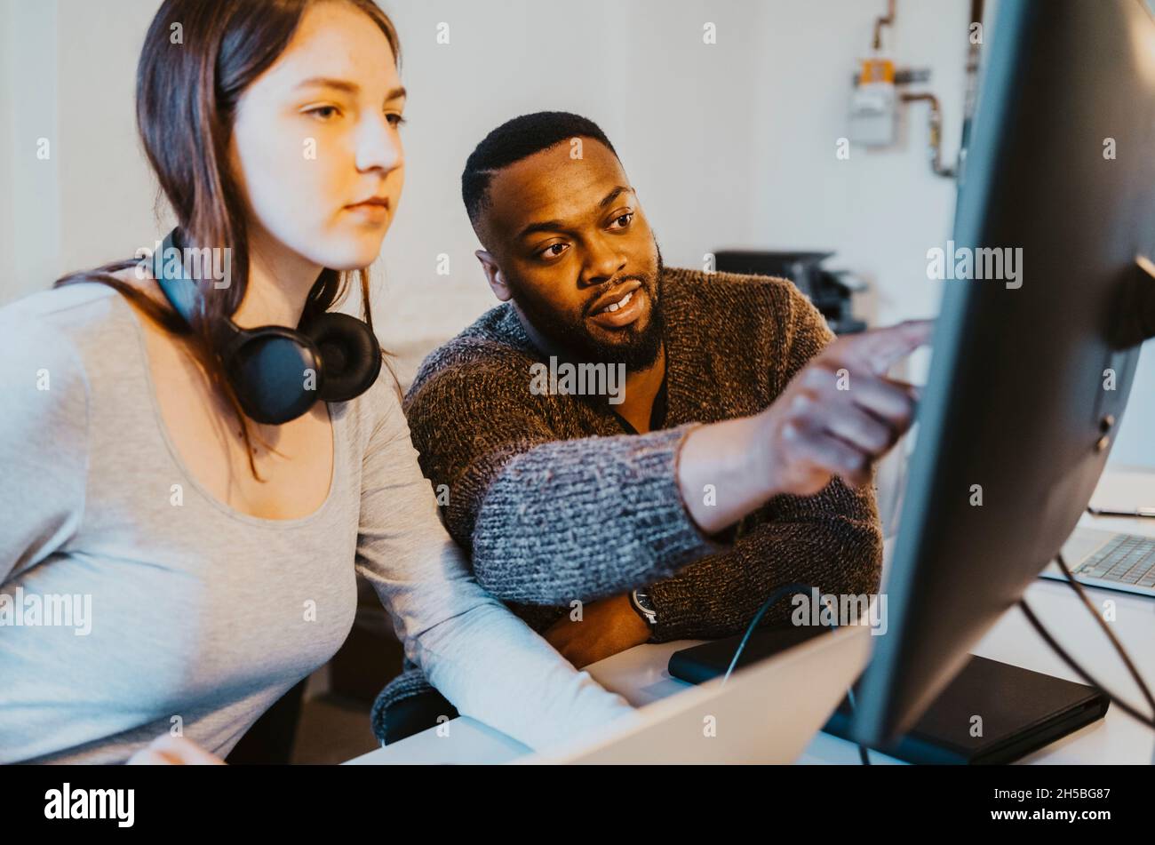 Hacker masculin discutant avec une collègue féminine sur l'ordinateur dans la société de démarrage Banque D'Images