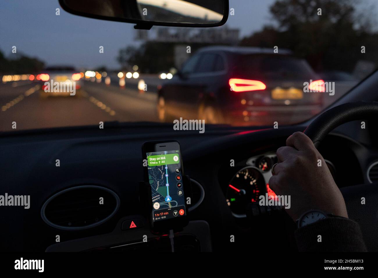 Vu du siège passager d'une voiture, la lumière d'hiver s'estompe dans l'obscurité à travers le pare-brise dont le conducteur utilise Google Maps pour se diriger vers l'est vers Londres sur l'autoroute M4, le 7 novembre 2021, à Londres, en Angleterre. Banque D'Images