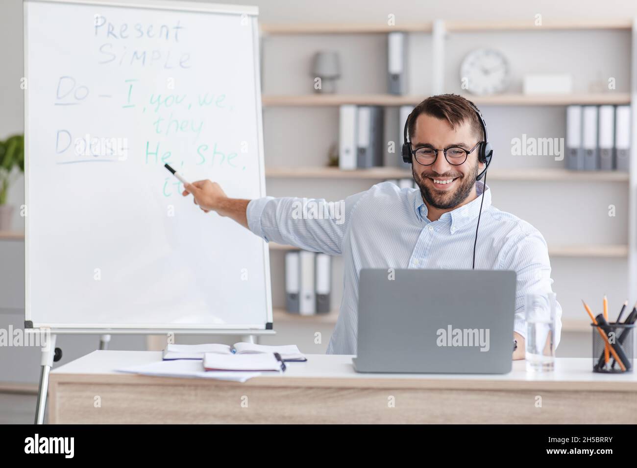 Souriant, homme de race blanche enseignant en lunettes, casque au tableau noir avec règles anglaises Banque D'Images