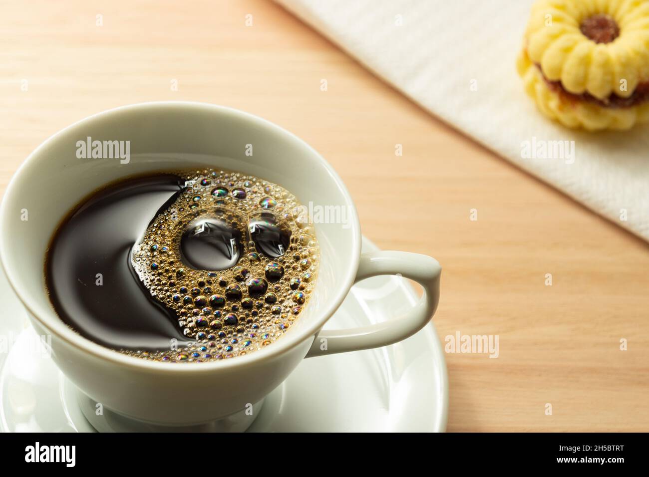 Une tasse blanche avec du café et un biscuit sur le bord de la soucoupe sur une surface en bois. Banque D'Images