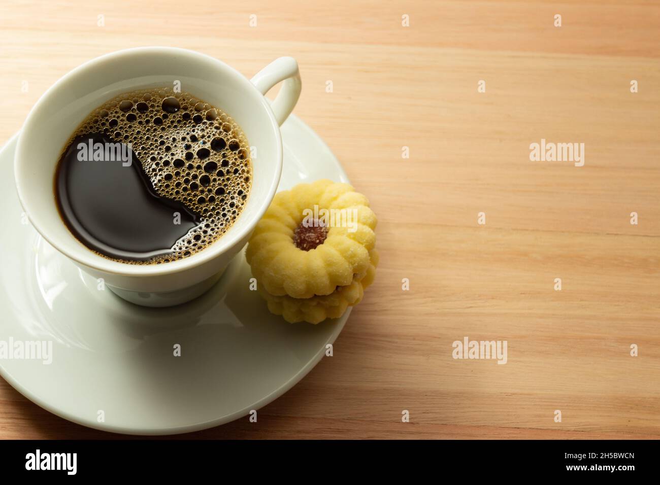 Tasse de café avec un biscuit de beury arrosé de sucre à l'intérieur de la soucoupe sur une surface en bois. Banque D'Images