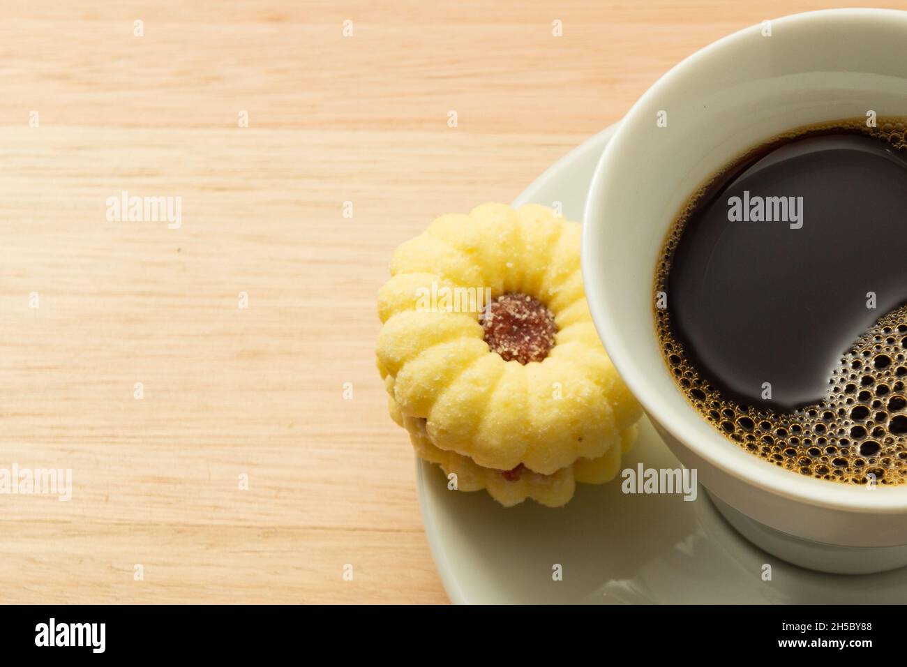 Tasse de café avec un biscuit de beury arrosé de sucre à l'intérieur de la soucoupe sur une surface en bois. Banque D'Images