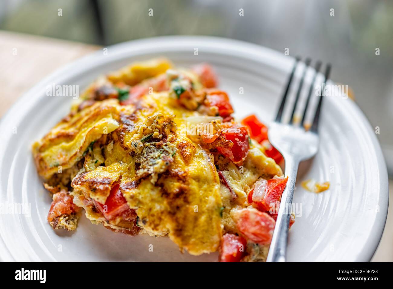 Macro-gros plan d'une assiette blanche maison avec omelette cuite prête à manger avec tomates, coriandre et poivrons rouges légumes sur table de cuisine en bois avec Banque D'Images