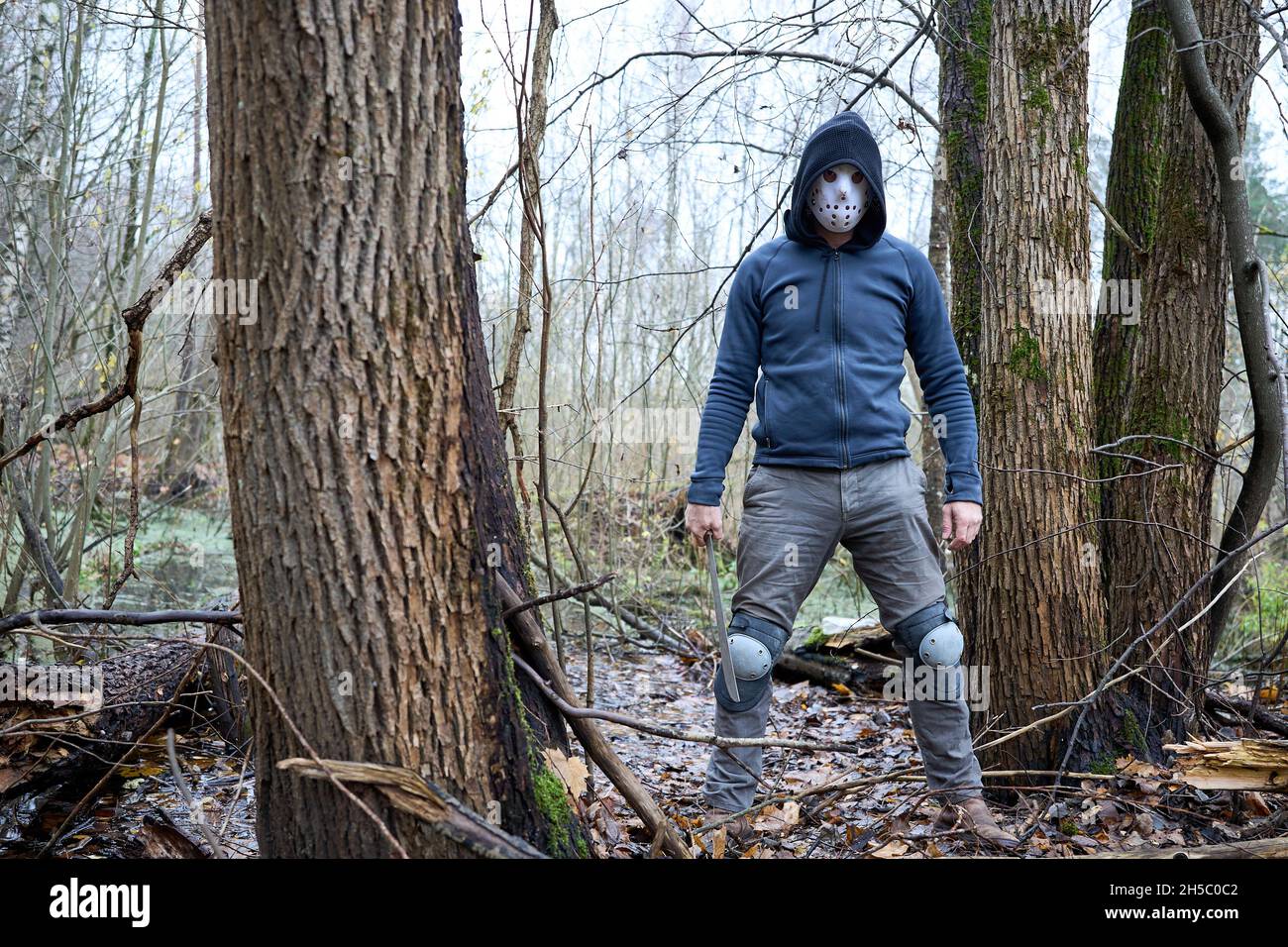 Tueur en série Jason Voorhees dans le masque de hockey et la machette restant dans le marais dans la forêt d'automne.Vendredi 13h Cosplay costume. Banque D'Images