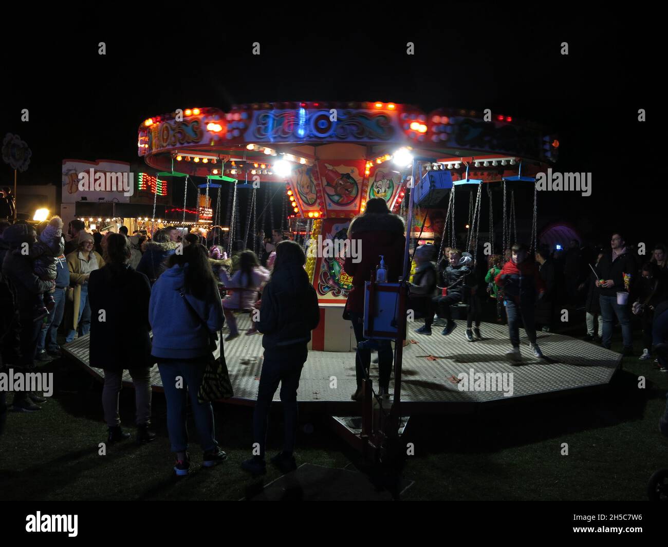 La nuit au Fun Fair et les parents se tiennent devant un joyeux tour pour les jeunes enfants ; Bonfire Night 2021, Wootton Fields Banque D'Images