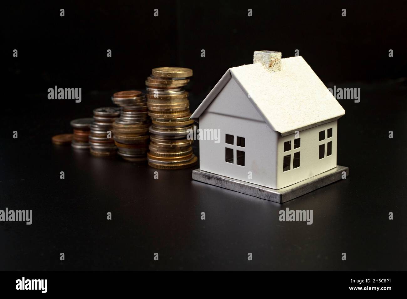 piles de pièces de monnaie croissant en hauteur, menant à une maison blanche miniature, sur fond noir, foyer sélectif Banque D'Images
