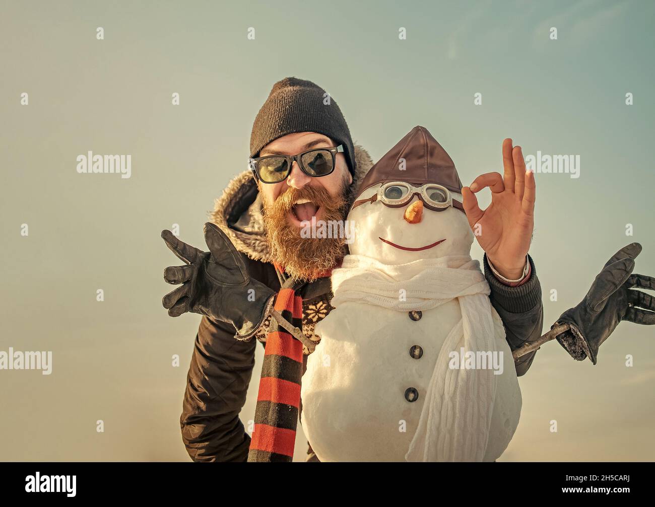Homme d'hiver avec bonhomme de neige dans un chapeau de pilote.Homme de Noël avec barbe sur le visage heureux.Pilote bonhomme de neige, fête des vacances d'hiver. Banque D'Images