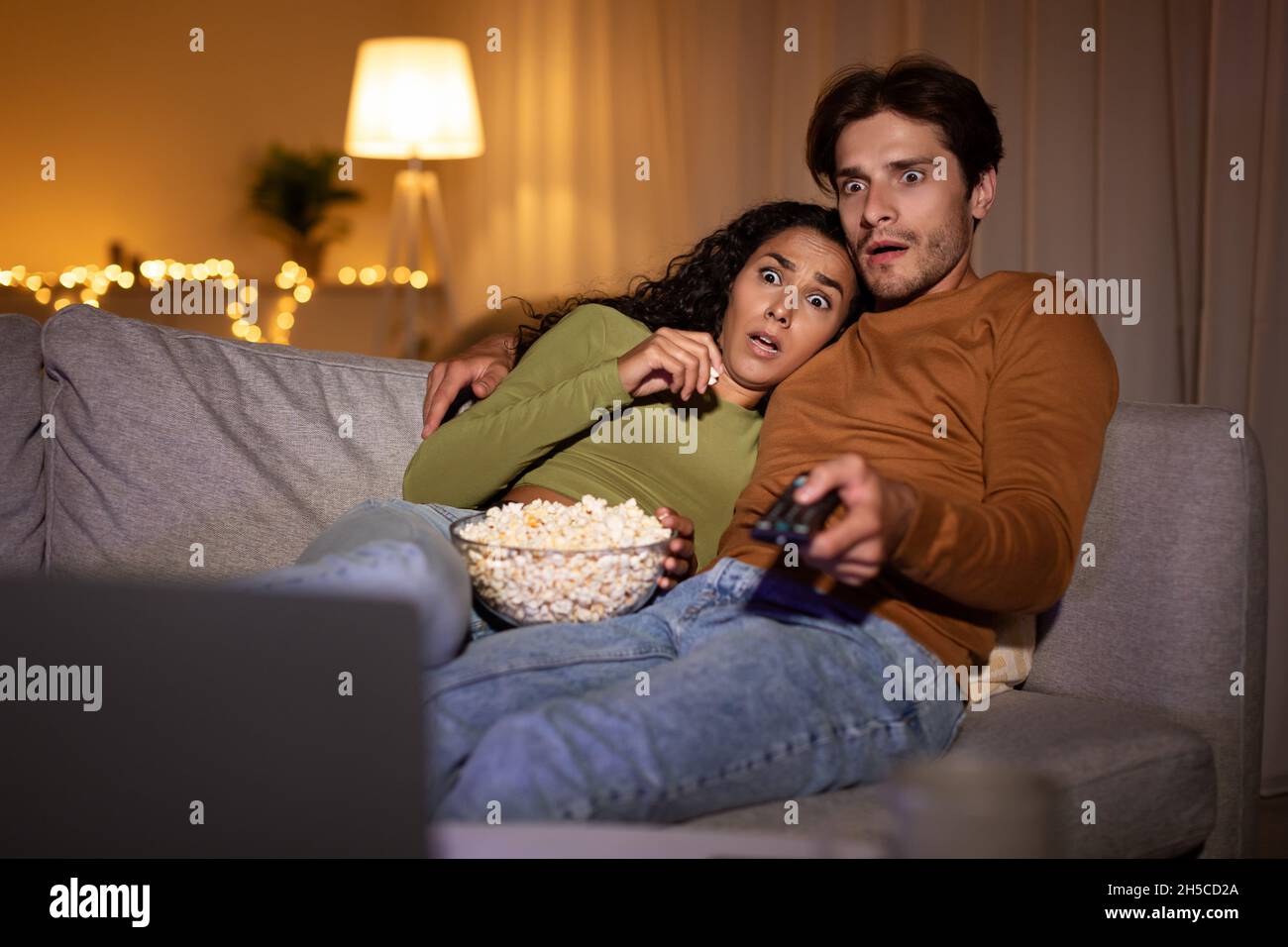 Un couple choqué regarde un film d'horreur à la télé à la maison Banque D'Images