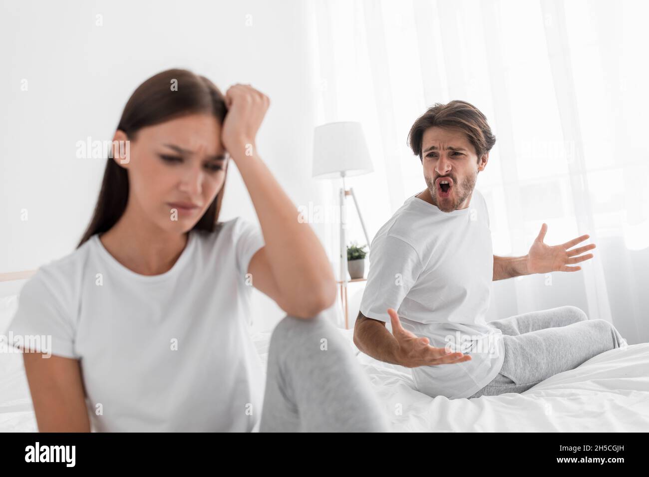 Agressif mal millénaire mari caucasien avec des cris de chaume et des essaims à offensé triste femme déprimée dans la chambre à coucher Banque D'Images