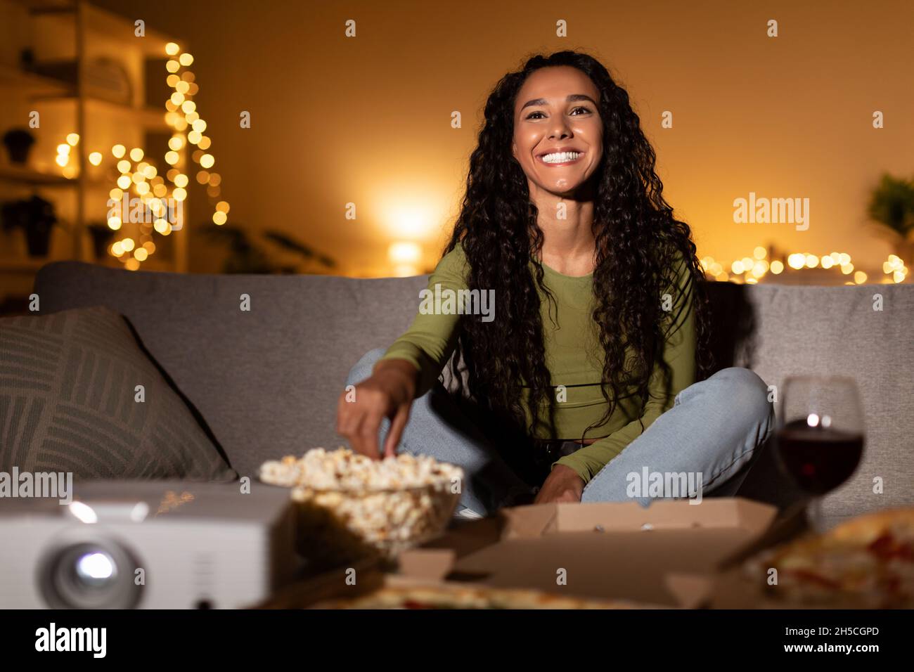 Femme millénaire regardant le film en ligne manger Popcorn Drinking vin intérieur Banque D'Images