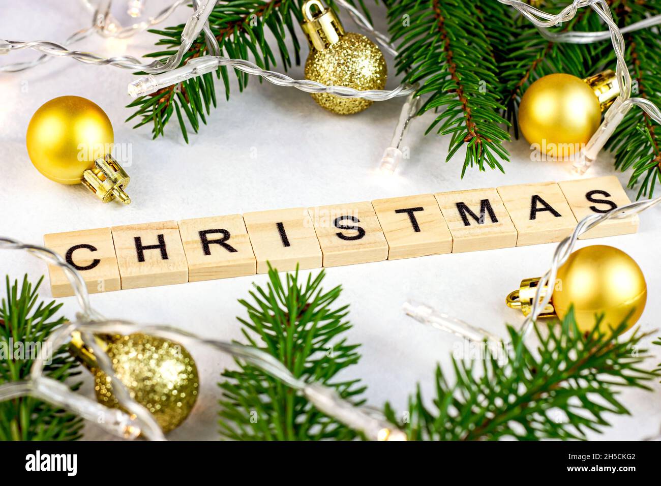 Texte de Noël en bois avec branches de sapin vert, boules dorées et lumières en tant que décorations saisonnières de Noël sur fond blanc pour cartes de vœux. Banque D'Images Texte de Noël en bois avec branches de sapin vert, boules dorées et lumières en tant que décorations saisonnières de Noël sur fond blanc pour cartes de vœux. Banque D'Images