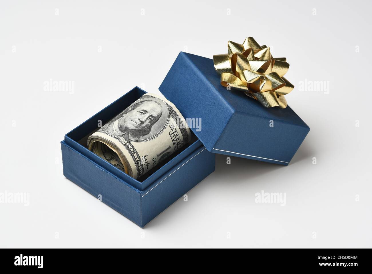 Une boîte cadeau bleue et un noeud doré avec un rouleau de billets de cent dollars. Banque D'Images