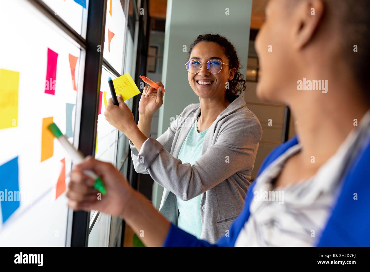 Femme d'affaires souriante avec un collègue qui planifie la stratégie d'affaires plutôt que des notes adhésives au bureau Banque D'Images