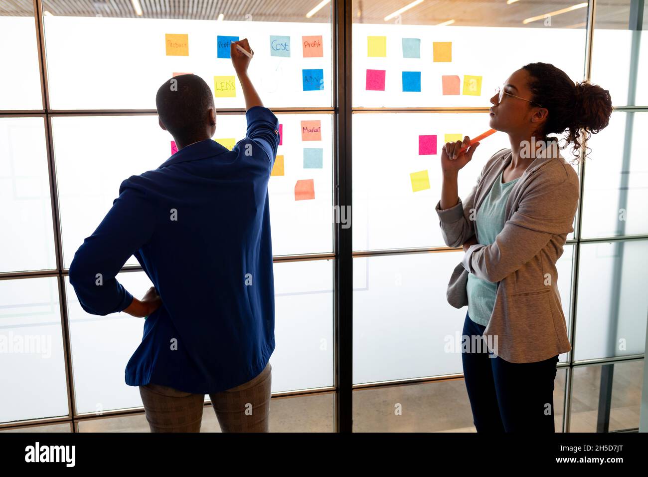 Les femmes d'affaires multiraciales remue-méninges sur des notes adhésives colorées dans un bureau créatif Banque D'Images