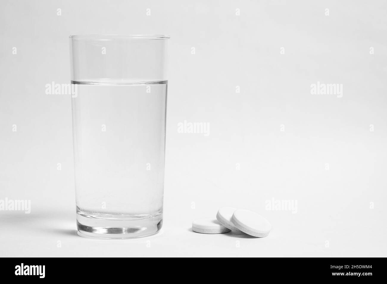 Verre d'eau propre et des pilules sur fond gris Banque D'Images