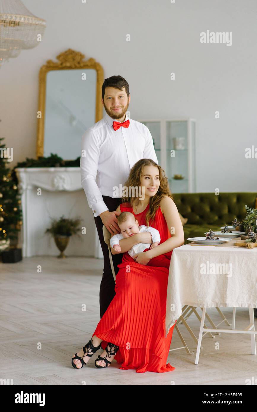 Parents Elegants Avec Un Bebe Dans Le Salon De Noel Maman S Assoit A La Table Et Tient Le Bebe Dans Ses Bras Papa Se Tient A Cote D Eux Photo Stock Alamy