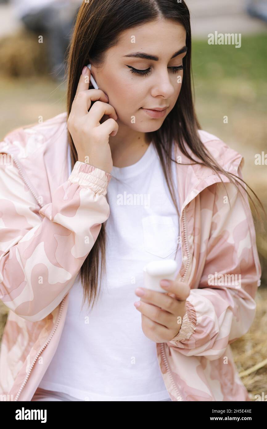 Une jeune femme met un casque sans fil dans les oreilles.Une femme tient le doigt par un casque et sourit.Portrait d'une femme attrayante.Lifestile Banque D'Images