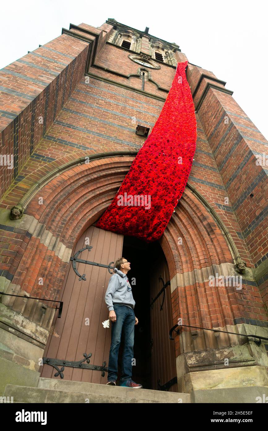 Cradley, West Midlands, Royaume-Uni.9 novembre 2021.Le gardien de l'église Paul Millward déverrouille les portes de l'église paroissiale de Saint-Pierre à Cradley, dans les West Midlands, tandis qu'une cascade de 75 mètres de coquelicots en maille orne la tour de l'église avant le dimanche du souvenir.Des milliers de coquelicots tricotés à la main ont été créés par les habitants de la région ainsi que par des contributeurs à l'étranger, et ont été l'enfant de Doreen Clifton, un résident de la région.Crédit : Peter Lophan/Alay Live News Banque D'Images