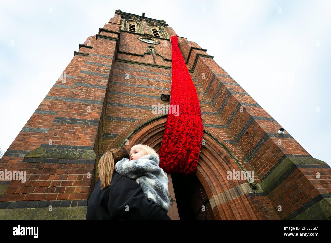 Cradley, West Midlands, Royaume-Uni.9 novembre 2021.Une résidente locale avec sa fille admire une cascade de coquelicots tricotés de 75 pieds qui orne la tour de l'église paroissiale de Saint-Pierre à Cradley, dans les Midlands de l'Ouest, avant le dimanche du souvenir.Des milliers de coquelicots tricotés à la main ont été créés par les habitants de la région ainsi que par des contributeurs à l'étranger, et ont été l'enfant de Doreen Clifton, un résident de la région.Crédit : Peter Lophan/Alay Live News Banque D'Images