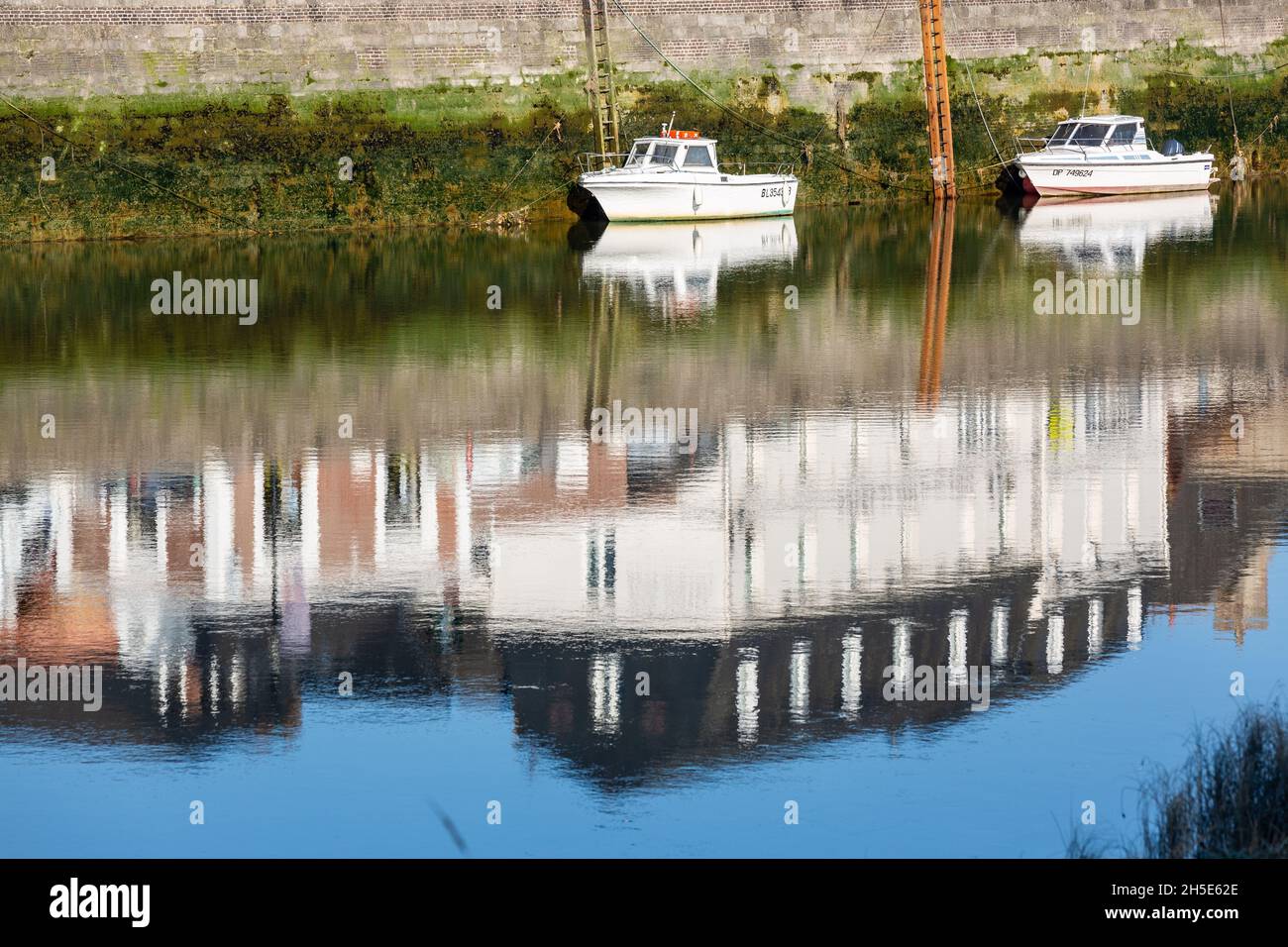 Petits bateaux de pêche amarrés à marée basse.Réflexions de maisons construites sur le quai.Saint-Valery, Baie de somme, France Banque D'Images