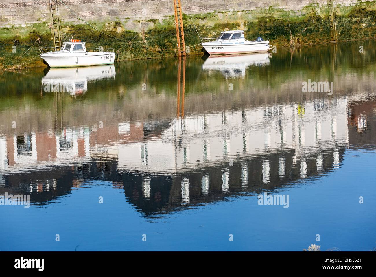 Petits bateaux de pêche amarrés à marée basse.Réflexions de maisons construites sur le quai.Saint-Valery, Baie de somme, France Banque D'Images