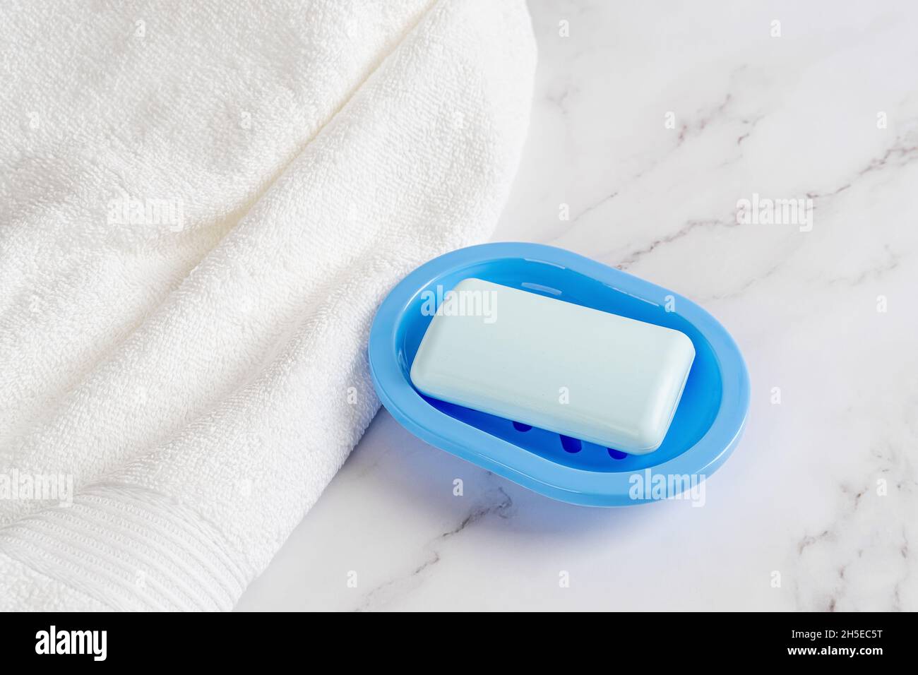 Porte-savon bleu clair sur un plat près d'une serviette en tissu éponge de coton blanc sur une surface en marbre.Se laver les mains avec du savon, de l'hygiène, de la pureté et des concepts de produits de toilette. Banque D'Images