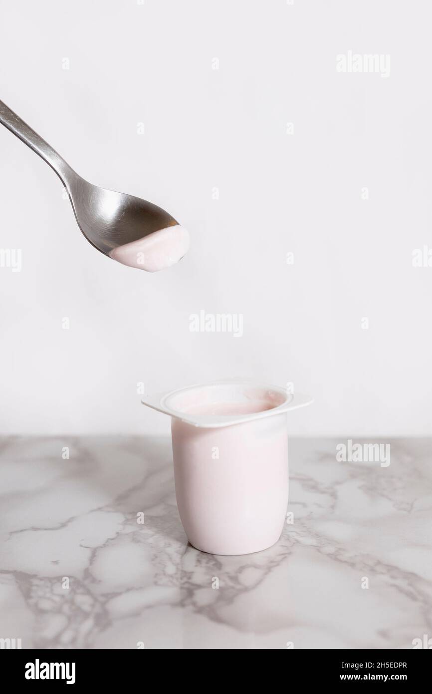 yaourt à la fraise sur une cuillère à café en métal avec un pot de yaourt  en plastique ci-dessous Photo Stock - Alamy