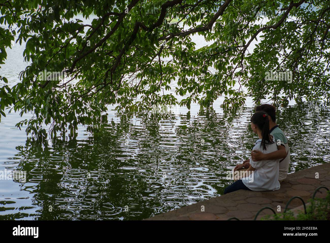 Un couple de jeunes amoureux se détendent sous les branches suspendues d'un arbre près des rives du lac Hoàn Kiem, Hanoi, Vietnam Banque D'Images