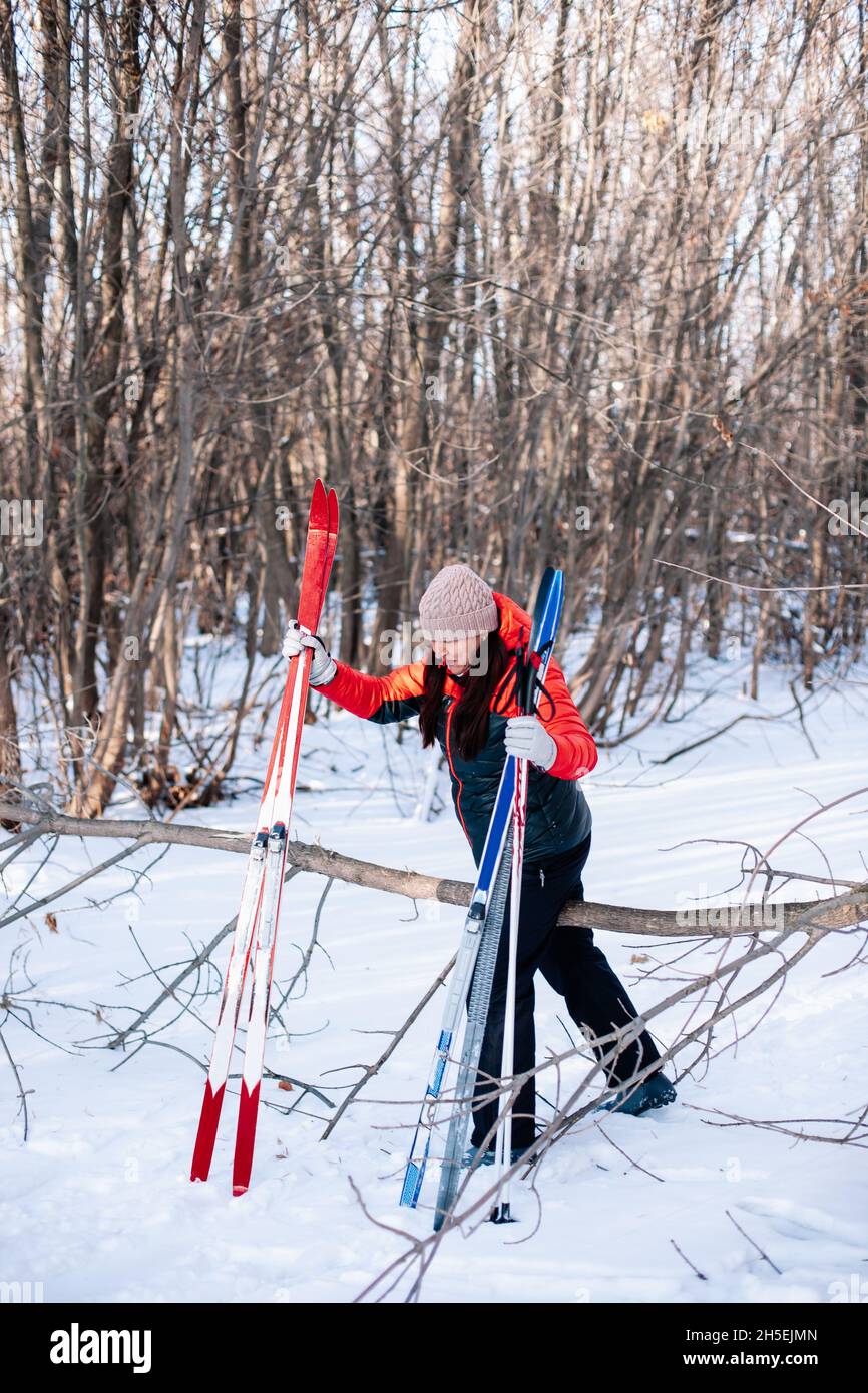 Une jeune femme marche dans la forêt.Brunette, en hiver, fait des promenades sur la route enneigée et tient des bâtons de ski et des skis entre ses mains Banque D'Images