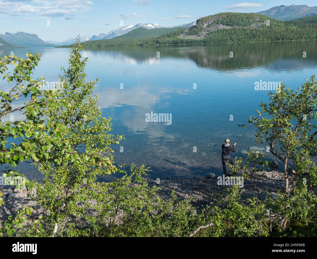 Pêcheur à la rivière Lule, dans un calme clair Lac de barrage de Lulealven eau douce à Saltoluokta en Suède Laponie à la belle journée d'été.Montagne rocheuse verte Banque D'Images