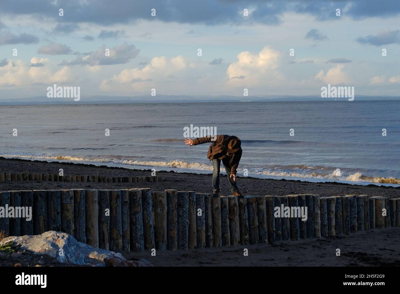 Un homme plus âgé qui se balance, qui marche sur une groyne en bois sur une plage. Banque D'Images