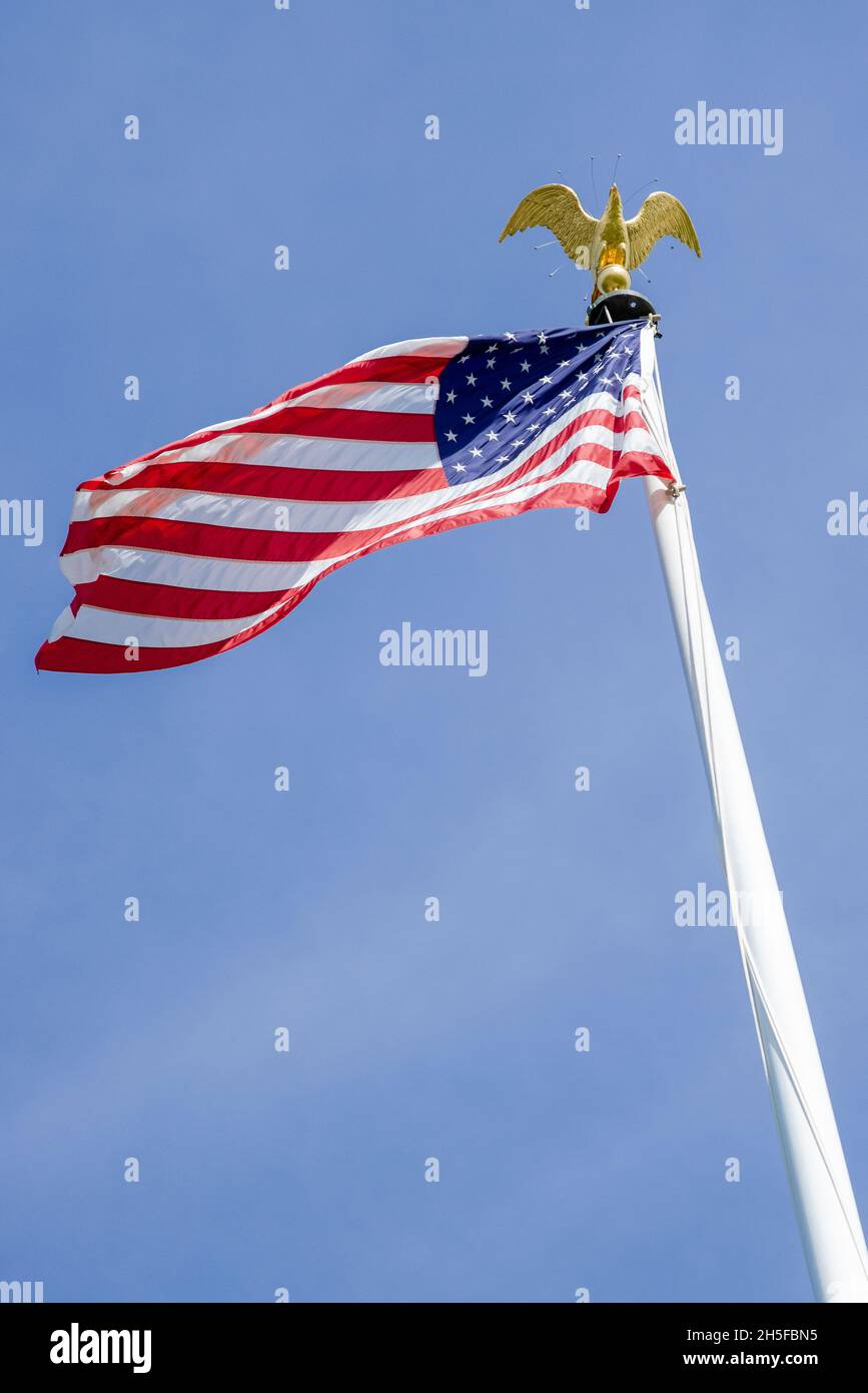 Drapeau américain agitant dans le vent contre un ciel bleu avec un aigle sur le poteau au cimetière de l'ABMC à Luxembourg, en Europe. Banque D'Images