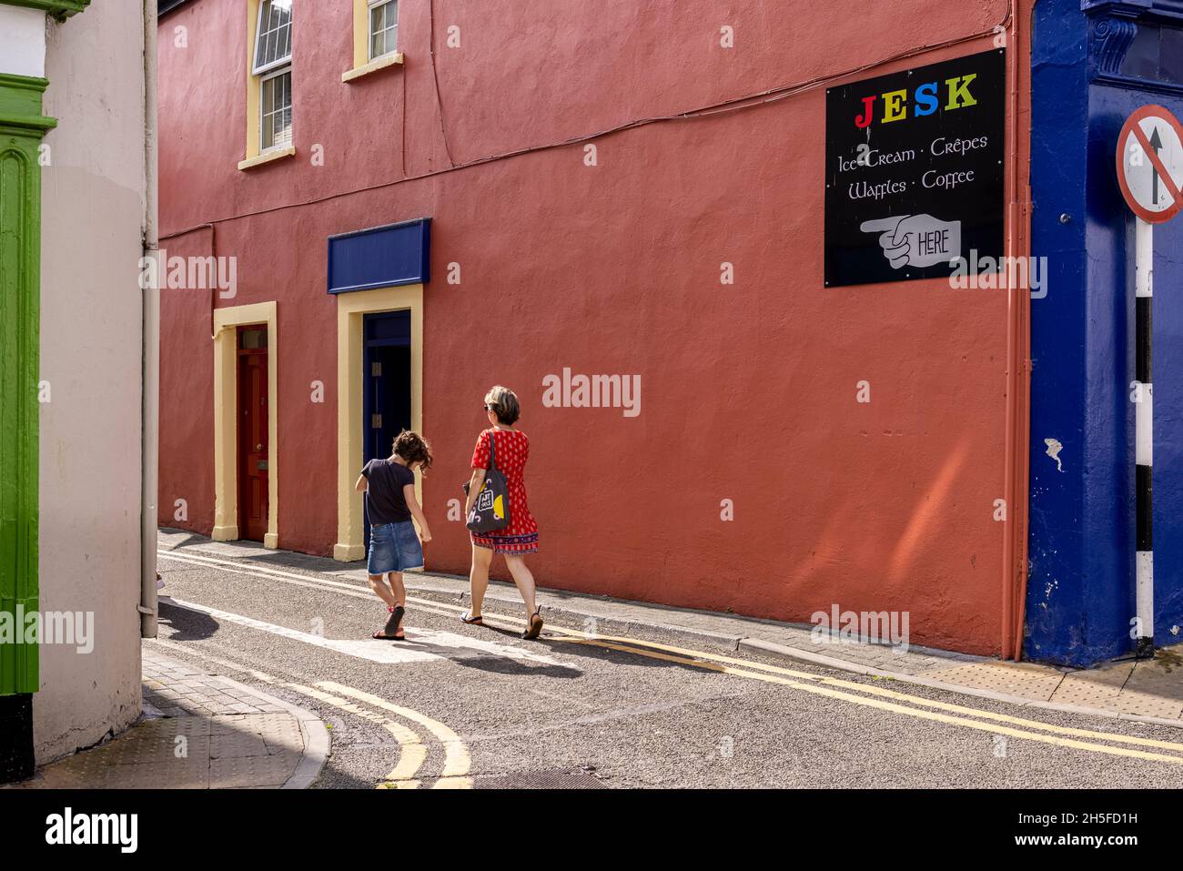 Scène de rue un matin d'été à Kinsale, femme en robe rouge et jeune fille dansant, Comté de Cork, Irlande Banque D'Images