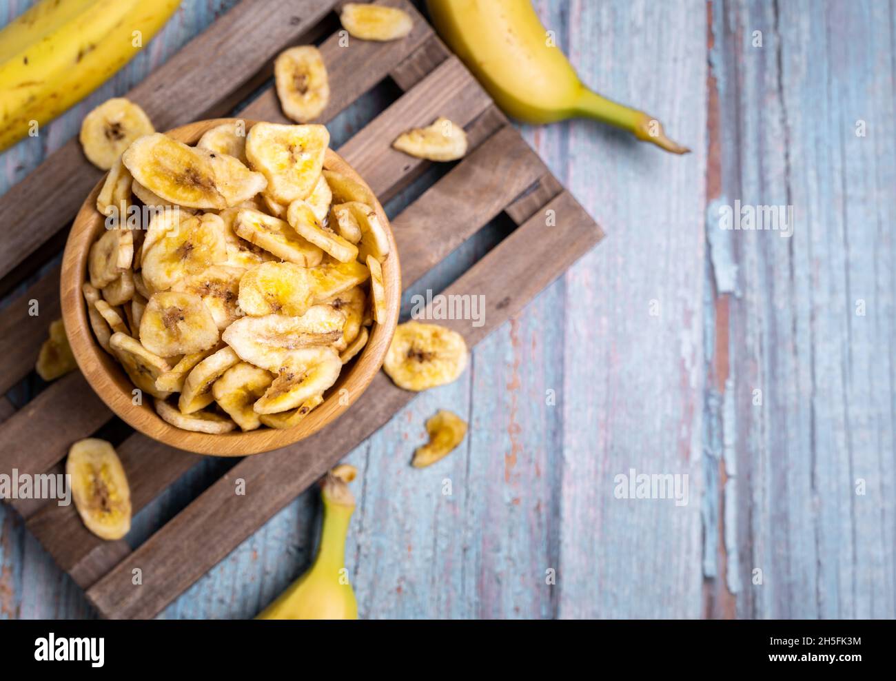 Vue de dessus des chips de banane biologique déshydratées sur le panneau en bois, décoré avec des bananes fraîches Banque D'Images