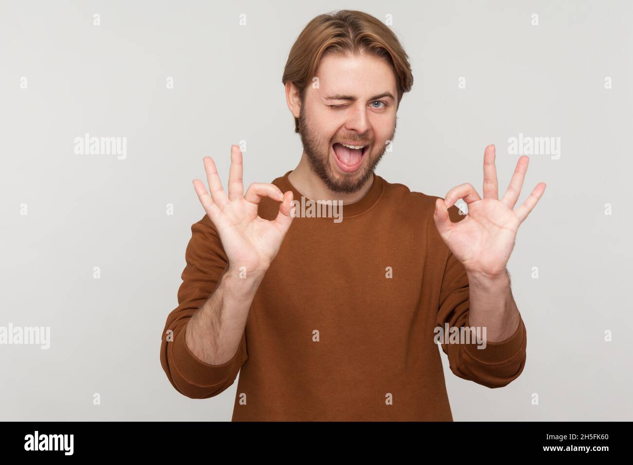 Portrait d'un homme avec une barbe portant un sweat-shirt, montrant un geste ok avec les doigts, approuvant le travail, satisfait de la qualité, regardant l'appareil photo.Prise de vue en studio isolée sur fond gris. Banque D'Images
