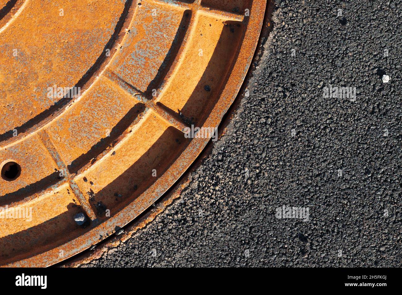 Trou d'égout rouge rouillé dans une route tarmac, fragment abstrait de gros plan Banque D'Images