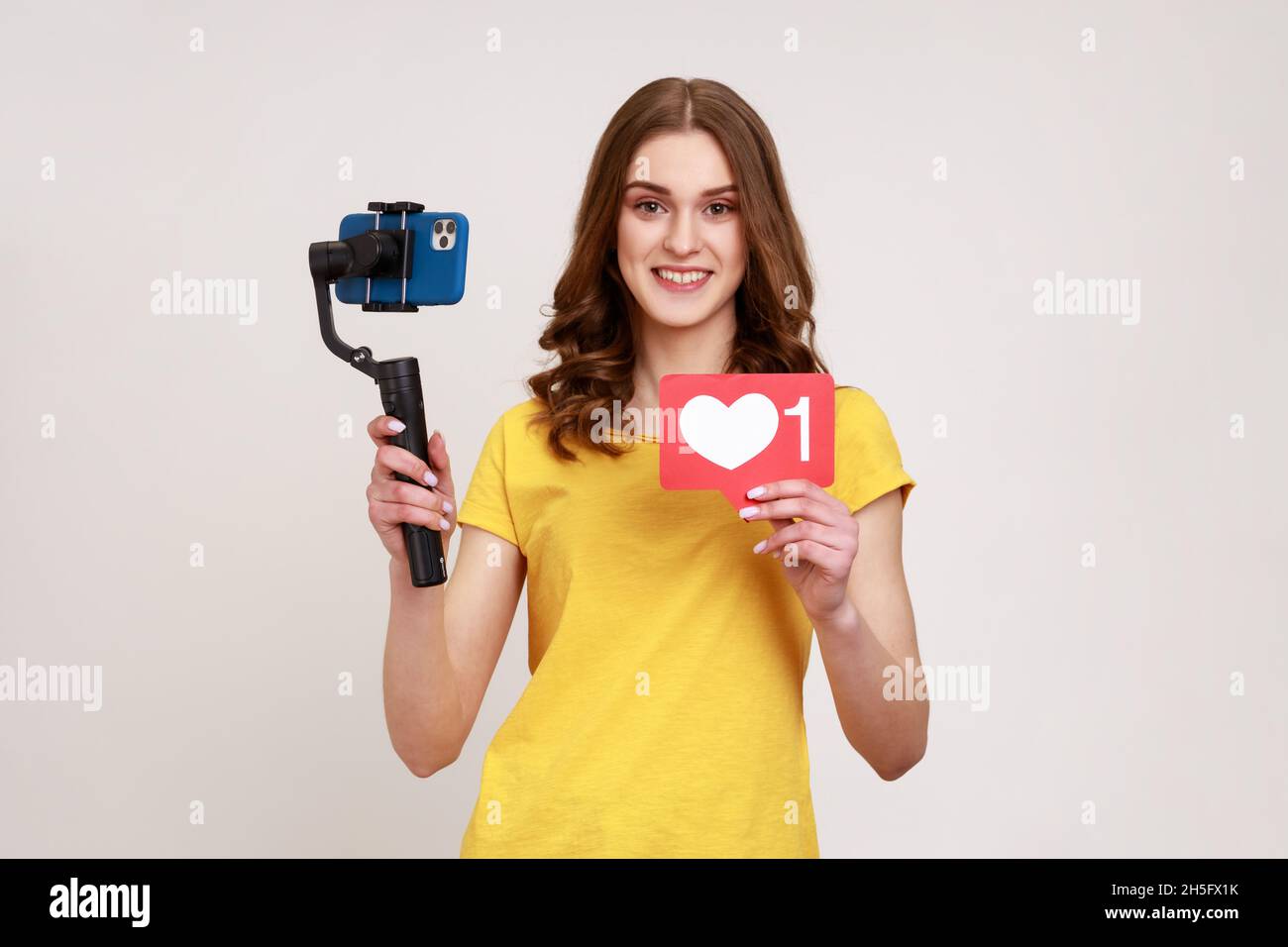 Une adolescente souriante se tourne sur un stabilisateur électronique pour le tournage de vidéos au téléphone, la diffusion en direct, se montrant comme une icône.Prise de vue en studio isolée sur fond gris. Banque D'Images