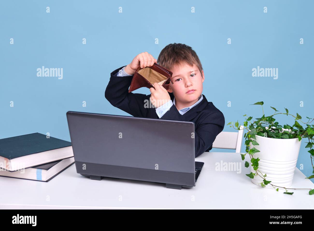 Un garçon dans un costume d'école avec un portefeuille vide, un espace de copie sur un fond bleu studio Banque D'Images