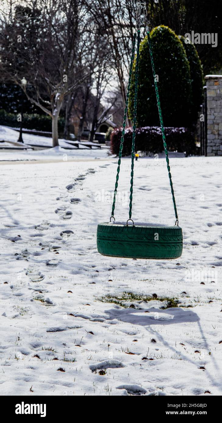 Balancement de pneu vert dans la cour de quartier dans la neige avec des ombres et des empreintes de pas menant de la cour de voisins à balancement. Banque D'Images