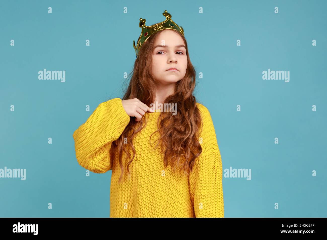 Petite princesse fille debout et pointant le doigt vers elle-même, regardant l'appareil photo avec confiance, portant jaune style décontracté pull.Studio d'intérieur isolé sur fond bleu. Banque D'Images