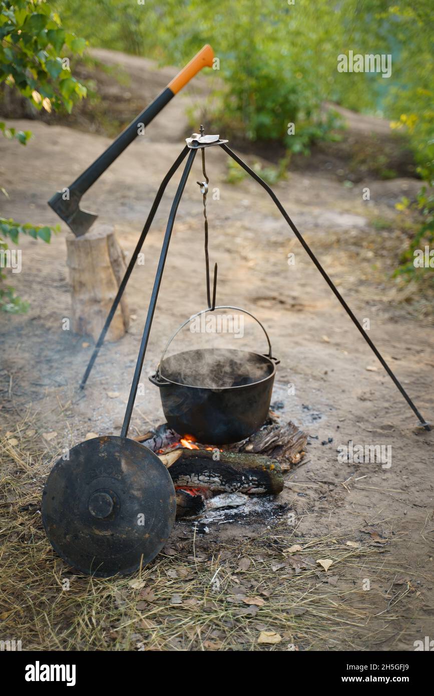 Un pot de camp, une hache, du bois de chauffage et un feu de camp.Préparer la nourriture sur feu de camp dans le camping sauvage, reposant sur la nature. Banque D'Images
